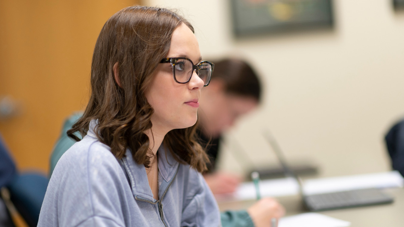 A female Dordt student with glasses sitting down looking forward paying attention to a lecture