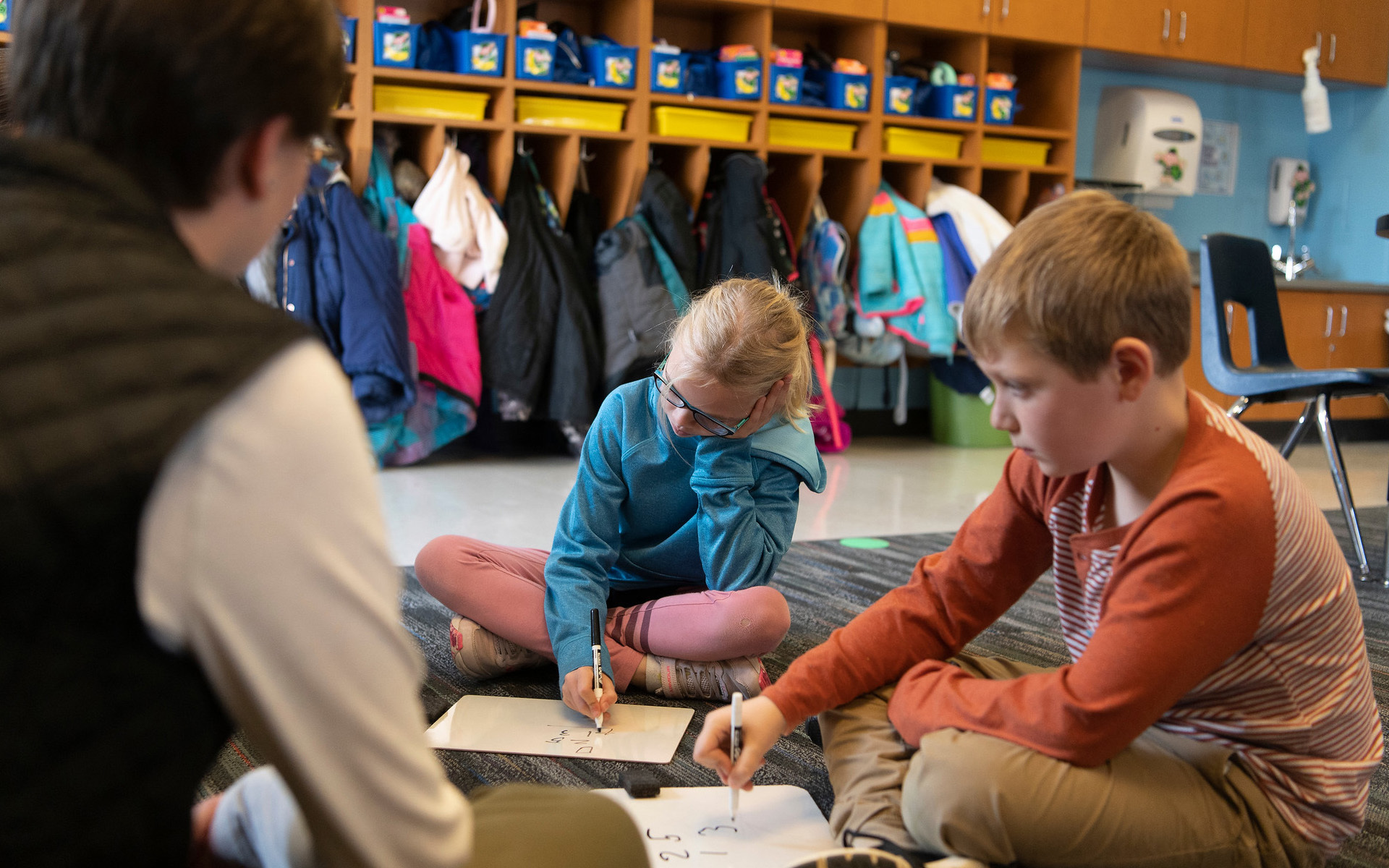 A Teacher sitting down watching as elementary students write on little white boards