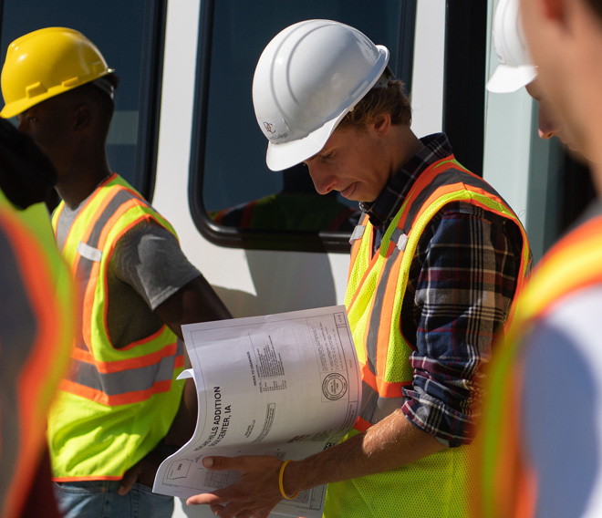 Dordt students in safety vests and helmets look at a construction plan packet