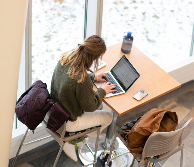 A Dordt student sitting down at a table working on her laptop