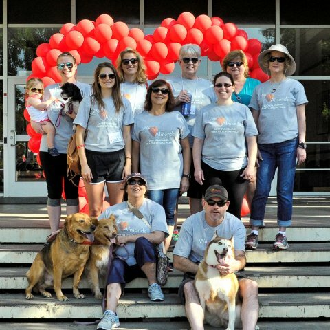 A group of people in matching shirts pose for a picture in front of a red balloon heart