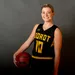 A picture of a smiling women wearing a basketball jersey and posing with a basketball in her hand.