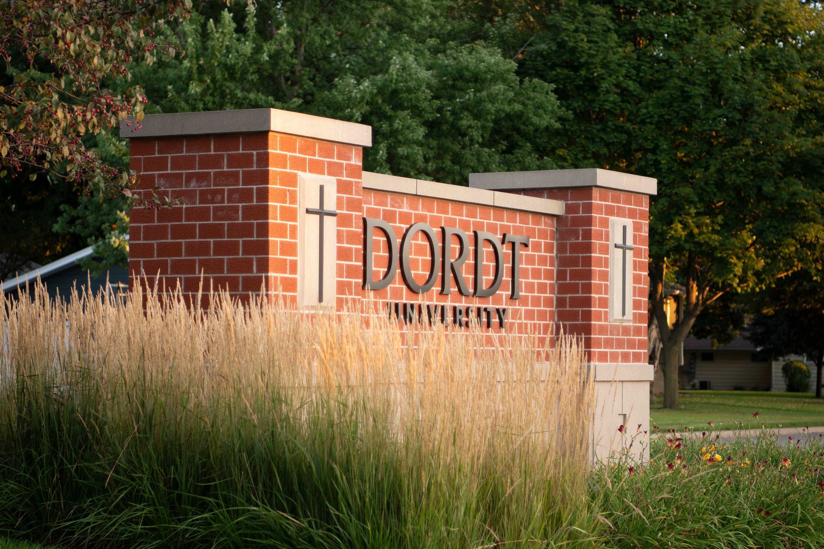 Brick and concrete sign of "Dordt University" is surrounded by prairie grass