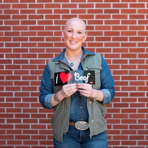 A smiling women holding up an "I heart beef" bumper sticker.