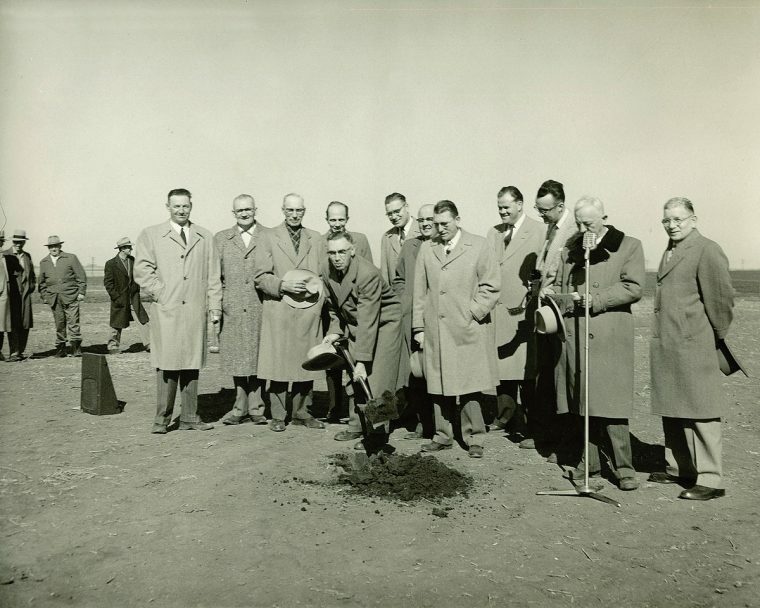 An old photo of a group of men in trench coats, with one digging a hole