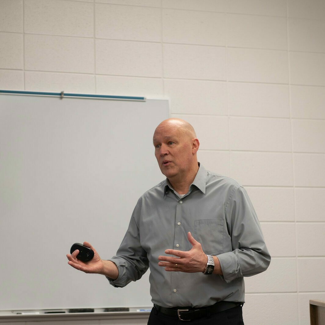 A picture of a professor holding a computer mouse while giving a lecture.