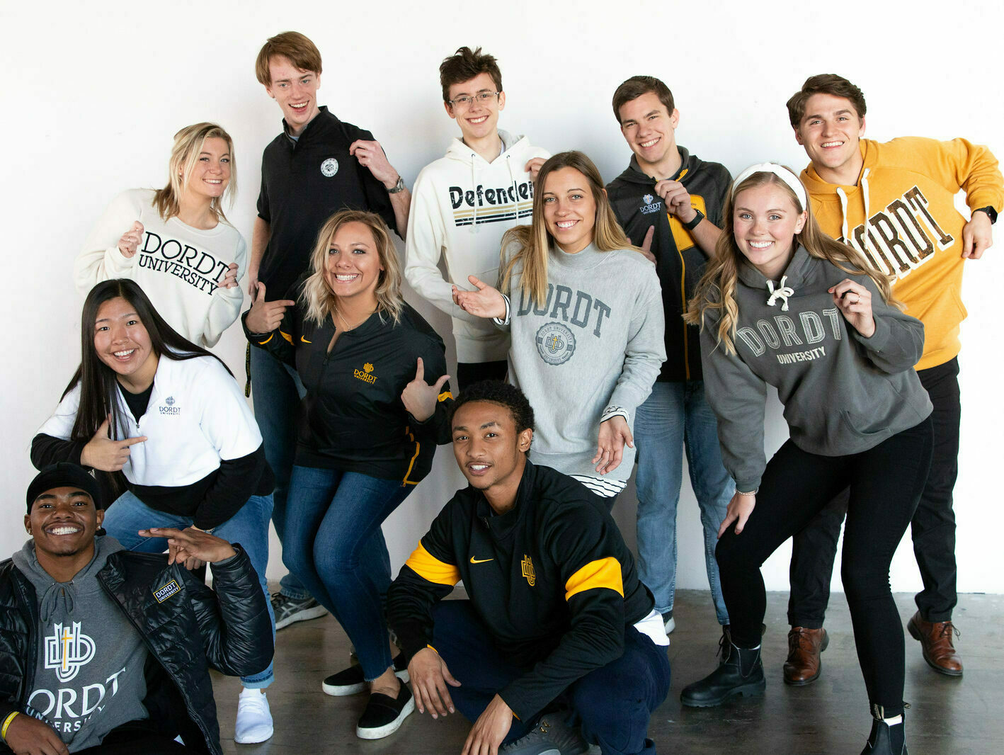 A picture of a group of smiling Dordt students pointing to the logos on their shirts.