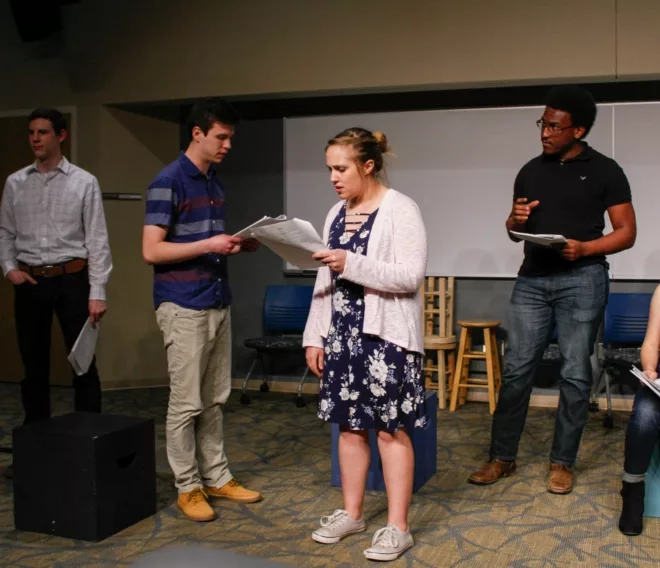 four theatre arts students read from scripts while practicing a scene