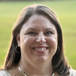 A smiling lady with gold necklace, sweater, and straight hair