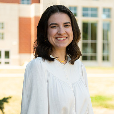 Smiling dark-haired young lady outside building