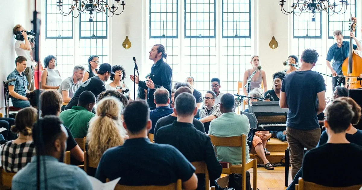 A gathering of attendees and instrumental performers in an airy space