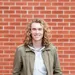 A picture of a man with long curly hair standing in front of a brick wall.