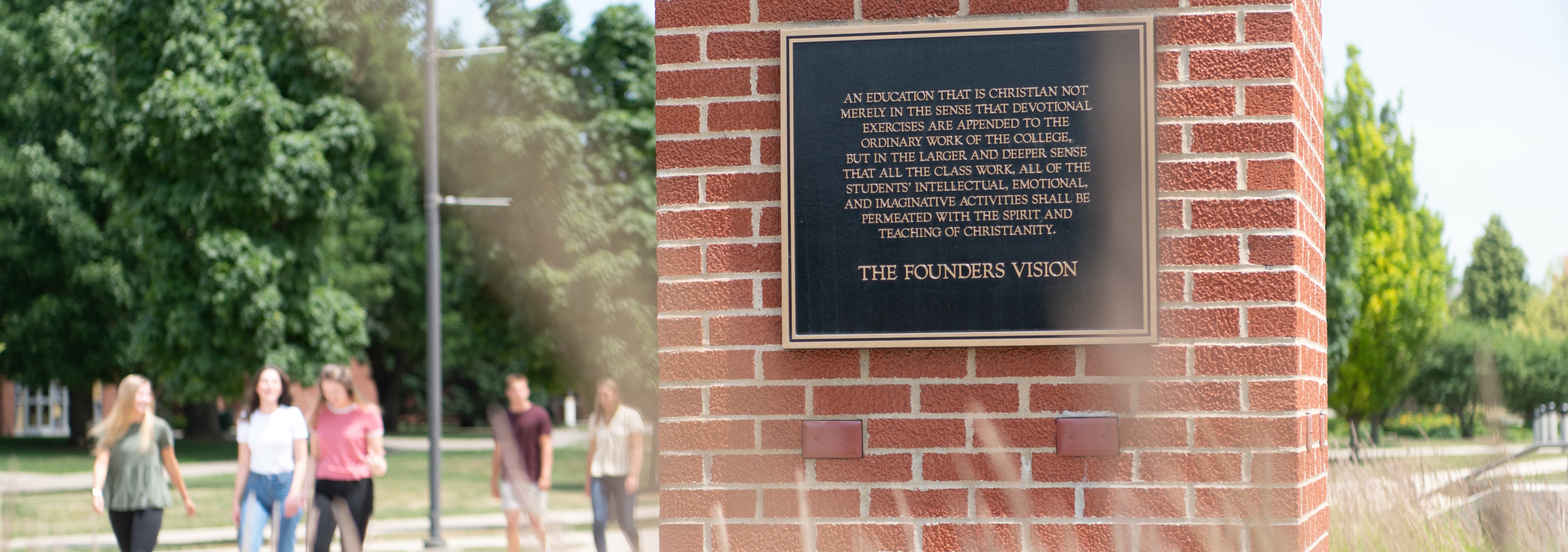 A picture of Dordt's founder's vision plaque with students walking in the background.