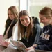 female student sitting on bench in window with laptop looks over to fellow students and smiles